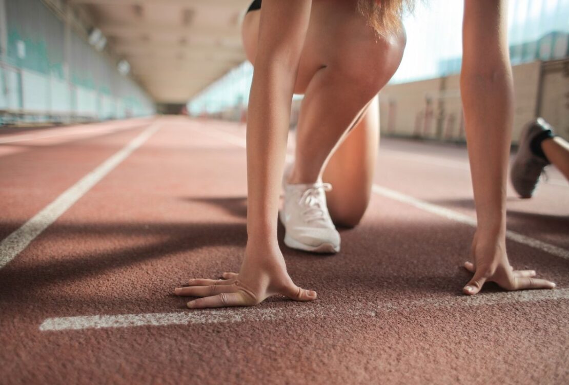 Uśmiechnięta kobieta w sportowym stroju biegnąca po parku, symbolizująca motywację do ćwiczeń i zdrowy styl życia.